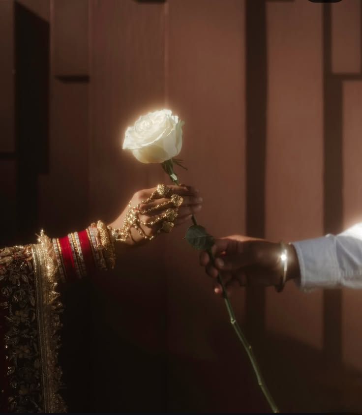 A mehendi-adorned bridal hand sharing a white rose